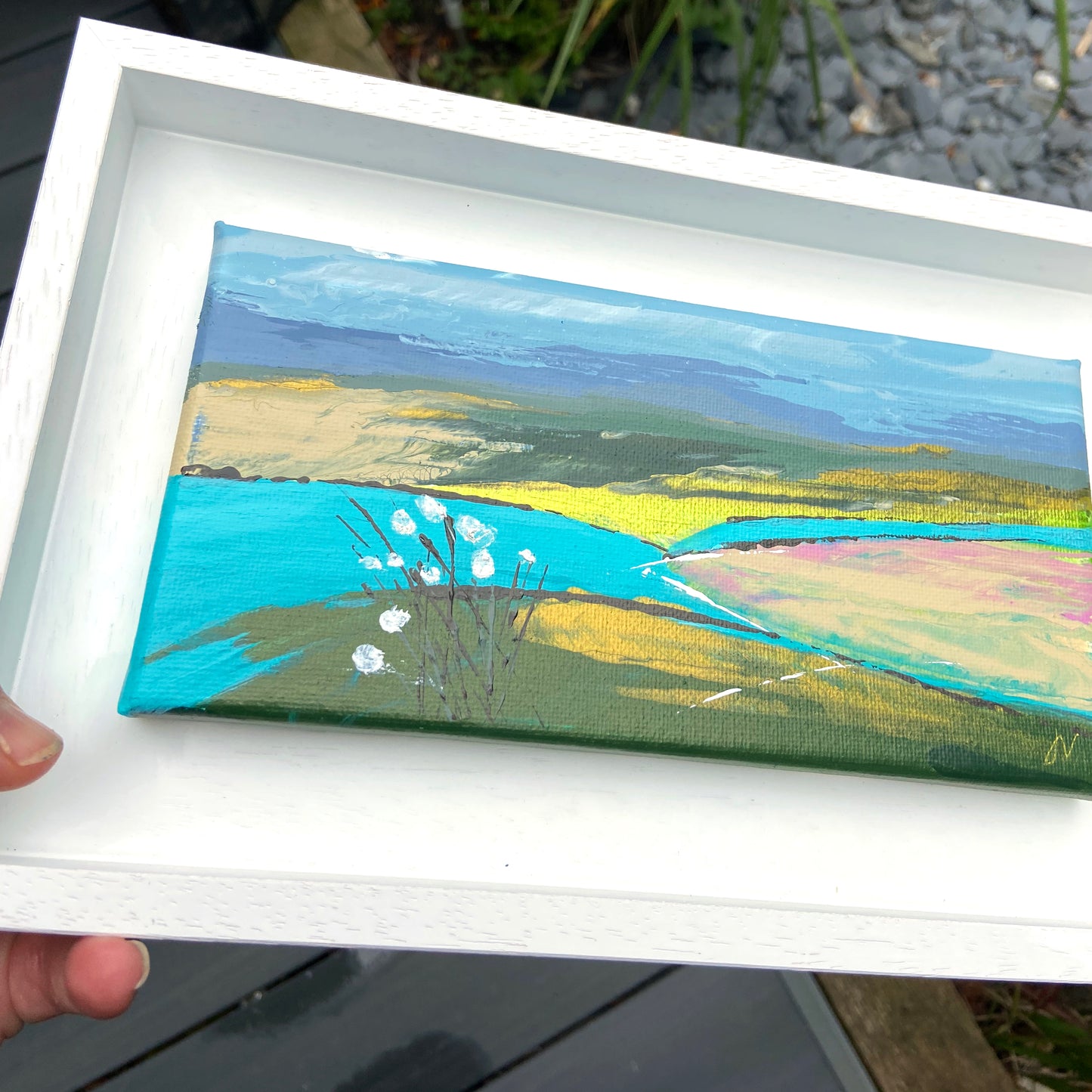 Small landscape painting held in a white frame